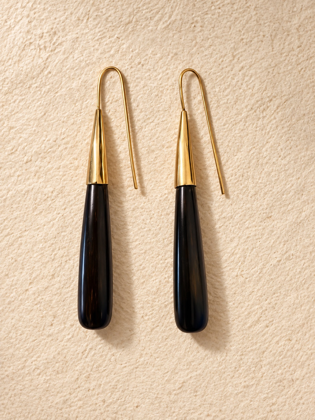 Noir Taper Earrings in polished cow horn and brass, photographed on a warm neutral background